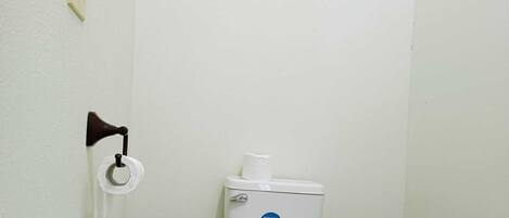 A small, clean bathroom with a toilet, a wall-mounted toilet paper holder, and a trash bin.