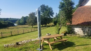 Een picknicktafel en een hoge, cilindervormige constructie in een grasrijk gebied, met een stenen muur en een gebouw met een rode pannendak op de achtergrond.