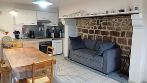 Een compacte keuken met witte kasten, een stenen muur, een grijze bank en een eettafel met stoelen.