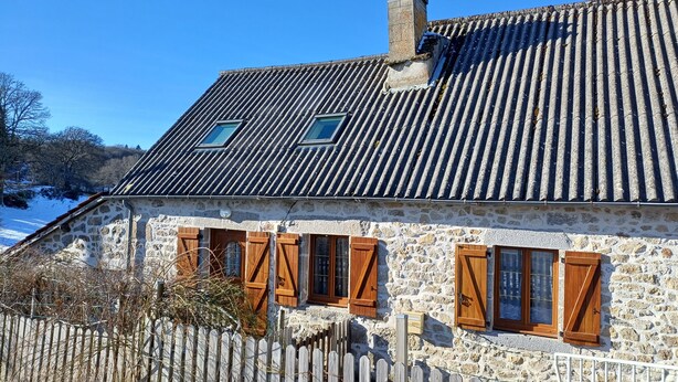 Een stenen huis met een pannendak, houten luiken en een schoorsteen.