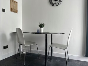 A modern dining area with a round table and two chairs, a wall-mounted clock, and a small potted plant. - Stockton-on-tees - 2 Beds - Pet Friendly - Parking (Stockton-on-Tees)