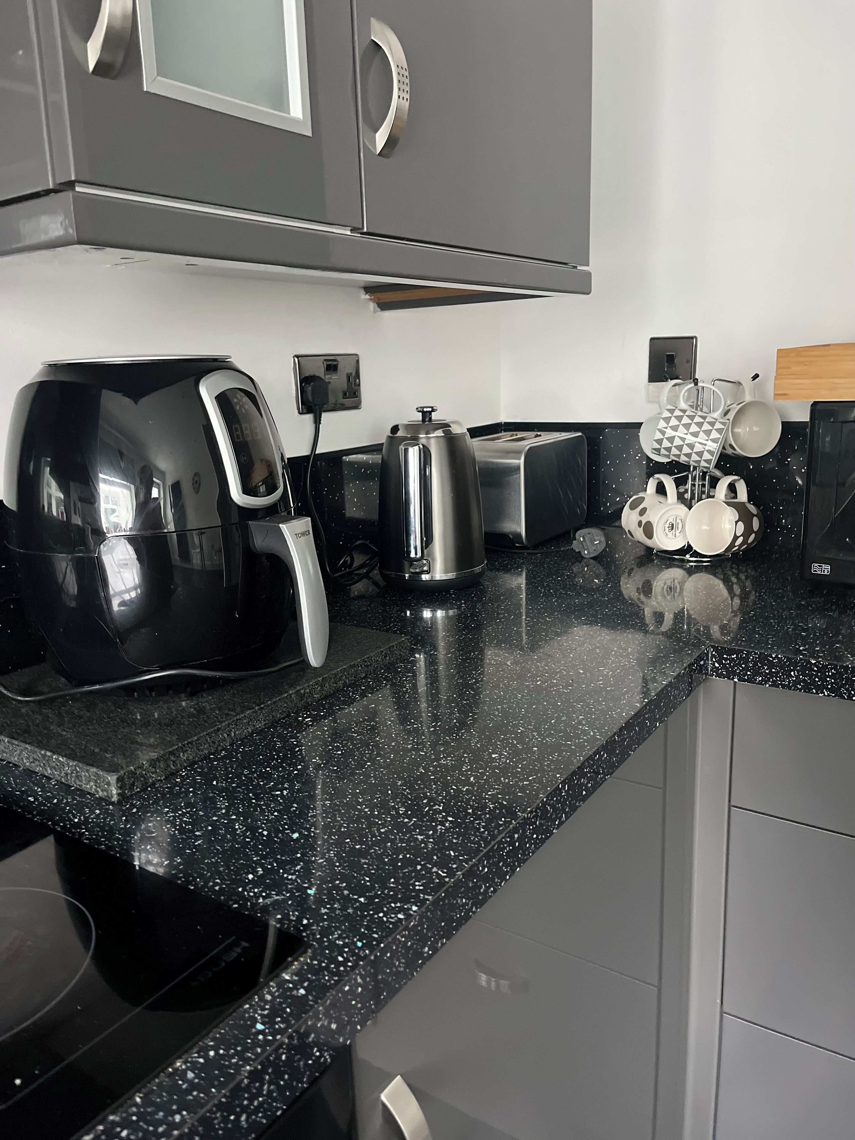 Une cuisine avec un plan de travail noir à motifs, une machine à café noire, une bouilloire, un grille-pain et un porte-tasses contenant des tasses à motifs.