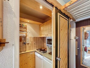 Compact kitchen with dishwasher, stove, and range hood, featuring a tiled backsplash and wooden ceiling.