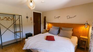 Un dormitorio con cama, cabecera de madera, mesitas de noche, lámpara colgante, armario y una puerta.