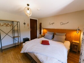 A bedroom with a bed, wooden headboard, bedside tables, a hanging light fixture, a wardrobe, and a door. - Mountain guest rooms, pets allowed (Ventron)