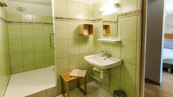 Un baño con baldosas verdes, un lavabo, un espejo, una ducha y un taburete de madera.