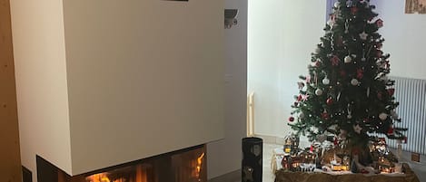Una sala de estar con chimenea, un árbol de Navidad y una puerta que da a otra habitación.