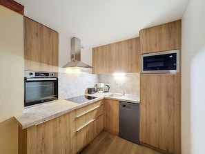A compact kitchen with wooden cabinets, a built-in oven, a microwave, and a dishwasher.