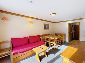A room with a wooden sofa, a small table, a wooden dining table, and a door leading to another room.
