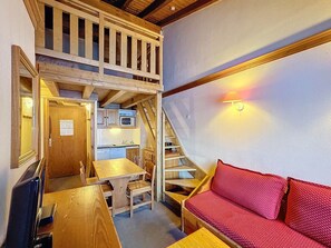 A compact room with a wooden table, a red sofa, a staircase leading to an upper level, and a kitchen area.