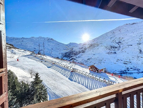 A snow-covered ski slope with a wooden viewing platform and a mountain in the background.
