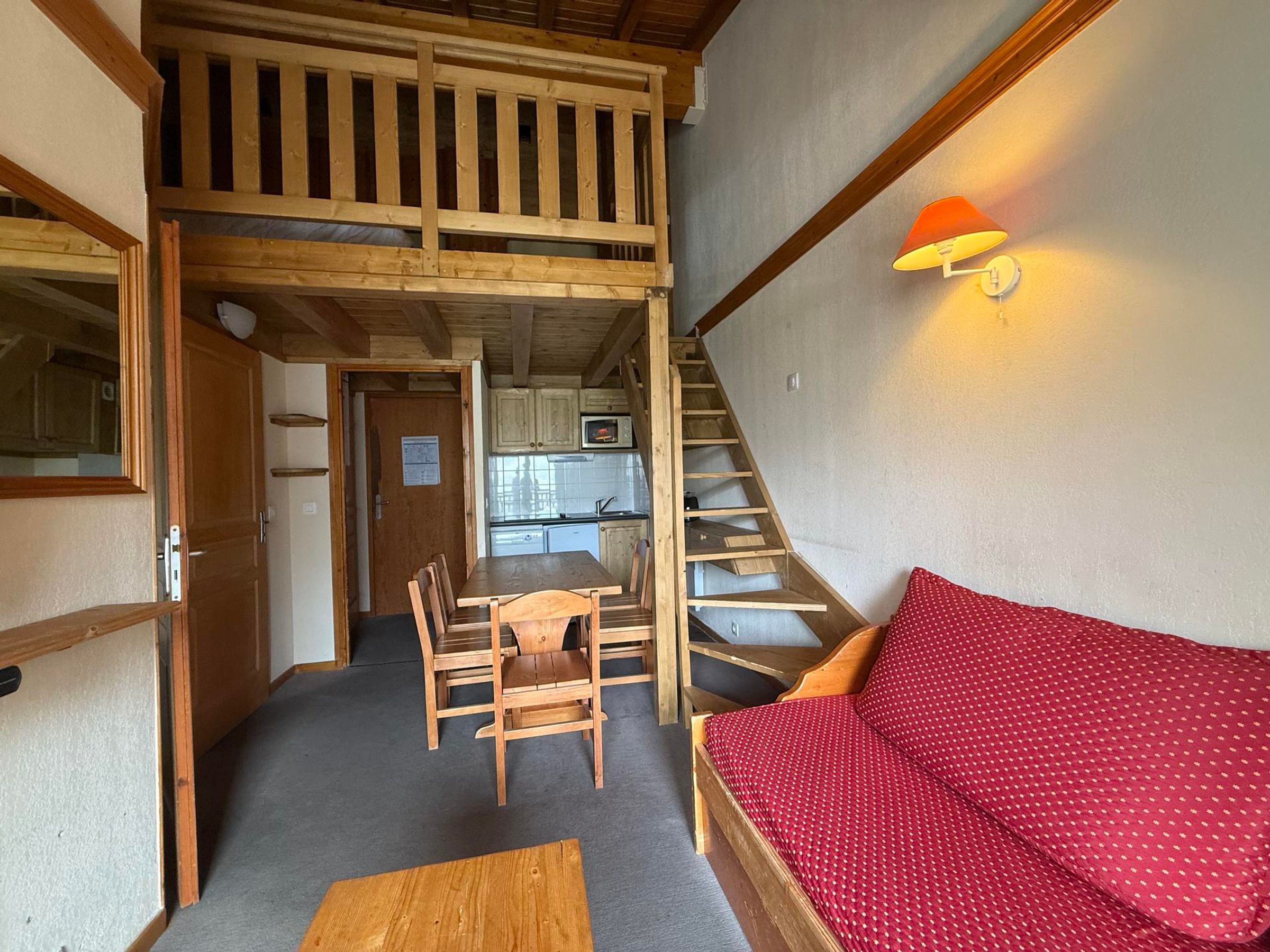 Una habitación pequeña con una cama litera de madera, una mesa de comedor con sillas, un sofá y una escalera.