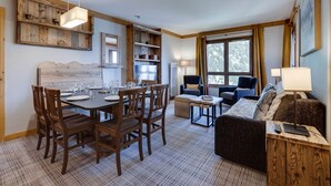 Une pièce chaleureuse avec une table à manger dressée pour quatre personnes, un canapé et une fenêtre avec des rideaux.