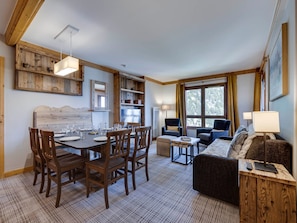 Une pièce chaleureuse avec une table à manger dressée pour quatre personnes, un canapé et une fenêtre avec des rideaux.