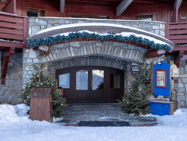 A stone archway leading to a wooden door with a Christmas tree and decorations on either side.