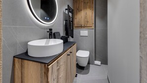 A modern bathroom with a round mirror, wooden cabinets, a toilet, and a towel rack. - Charming Apartment in Val d'Isère Center - 4 Guests, Balcony, WiFi (Val-d'Isère)