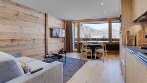 A modern interior with a wooden wall, a dining area with a view of mountains, and a kitchen with wooden cabinets. - Charming Apartment in Val d'Isère Center - 4 Guests, Balcony, WiFi (Val-d'Isère)
