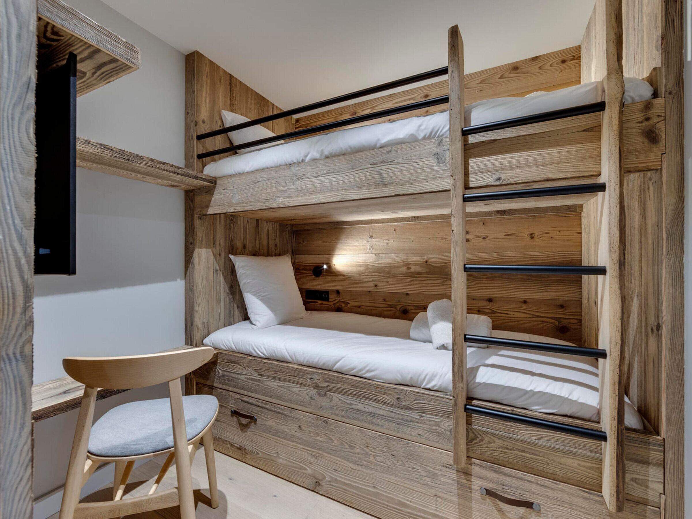 Ein Stockbett mit Holz-Kopf- und Fußteil, ein kleiner Holzhocker und ein Nachttisch.
