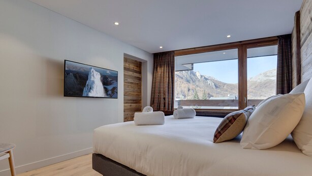 A modern bedroom with a large bed, a view of mountains, a wooden accent wall, and a painting of a mountain. - Charming Apartment in Val d'Isère Center - 4 Guests, Balcony, WiFi (Val-d'Isère)