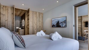 A modern hotel room with a large bed, wooden walls, a mounted picture, and a visible bathroom area. - Charming Apartment in Val d'Isère Center - 4 Guests, Balcony, WiFi (Val-d'Isère)