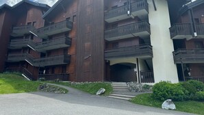 A multi-story building with wooden exterior and balconies, featuring a central entrance with steps and a stone pathway leading to the entrance. - Charming duplex for 5 near Blue Lake (Morillon Village)