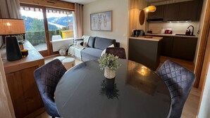 Ett mysigt vardagsrum med en soffa, ett matbord med stolar, ett kök med diskho och spis samt ett stort fönster med utsikt över omgivningen.