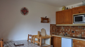 Une cuisine compacte avec des meubles en bois, un four à micro-ondes, un évier et une petite table à manger avec des chaises.