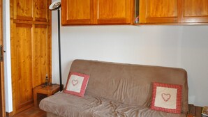 Une pièce avec une armoire en bois, un canapé agrémenté de coussins à carreaux et un lampadaire.