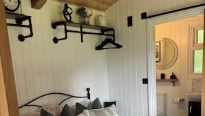 Ein ordentlich bezogenes Bett mit einer karierten Decke, ein Nachttisch mit einer Lampe und eine Wanduhr.