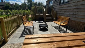 Eine Holzterrasse mit Bänken und einem Feuerkorb, die zu einem Gebäude mit Fenstern und einer Tür führt.