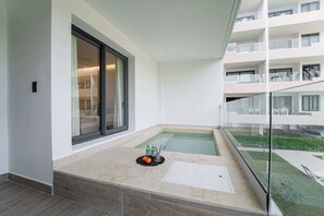 A modern balcony with a glass railing, a small pool, and a seating area with a mat and two bottles. - Beautiful new beach apartment (Punta Cana)