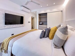A modern bedroom with a large bed, a TV mounted on the wall, a wardrobe, and a ceiling fan. - Beautiful new beach apartment (Punta Cana)