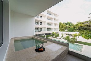 A modern hotel room with a balcony overlooking a swimming pool and a lush garden. - Beautiful new beach apartment (Punta Cana)