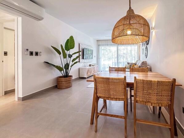 A modern dining area with a round table and wicker chairs, a potted plant, and a hanging light fixture. - Beautiful new beach apartment (Punta Cana)