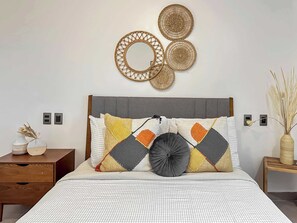 A bedroom with a bed, a wooden nightstand, a bedside table, and wall decor.