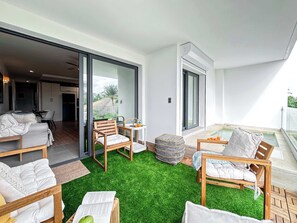 Una sala de estar moderna con piso de césped artificial verde, muebles de madera y vista al exterior.