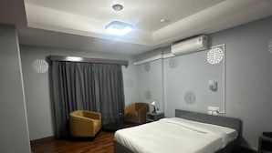 A modern hotel room with a large bed, wooden flooring, a seating area with two chairs, and an air conditioning unit on the wall. - The Gochukha Hotel (Thimphu)