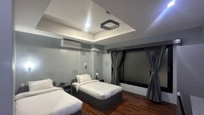 A modern hotel room with two beds, a large window with curtains, a ceiling light, and a wall-mounted air conditioner. - The Gochukha Hotel (Thimphu)