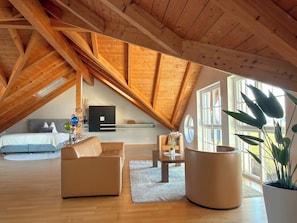 Un espacioso dormitorio tipo loft con techo inclinado, una cama, un sofá, una mesa de centro y una planta en maceta.