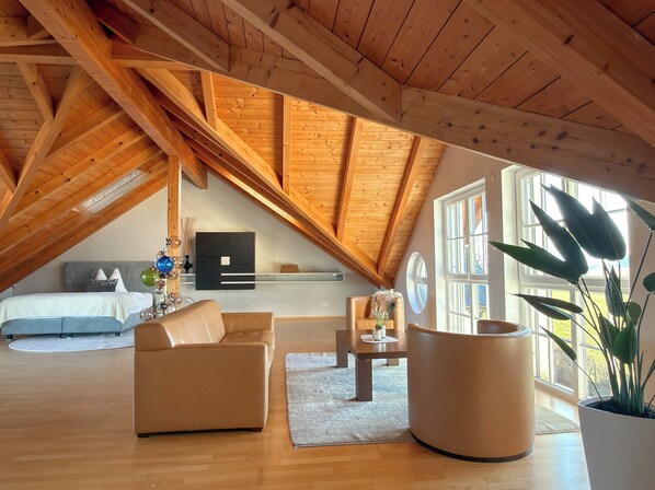 Un espacioso dormitorio tipo loft con techo inclinado, una cama, un sofá, una mesa de centro y una planta en maceta.
