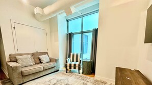 Ein Wohnzimmer mit Sofa, Sessel, einem gemusterten Teppich und einem großen Fenster mit Vorhängen.