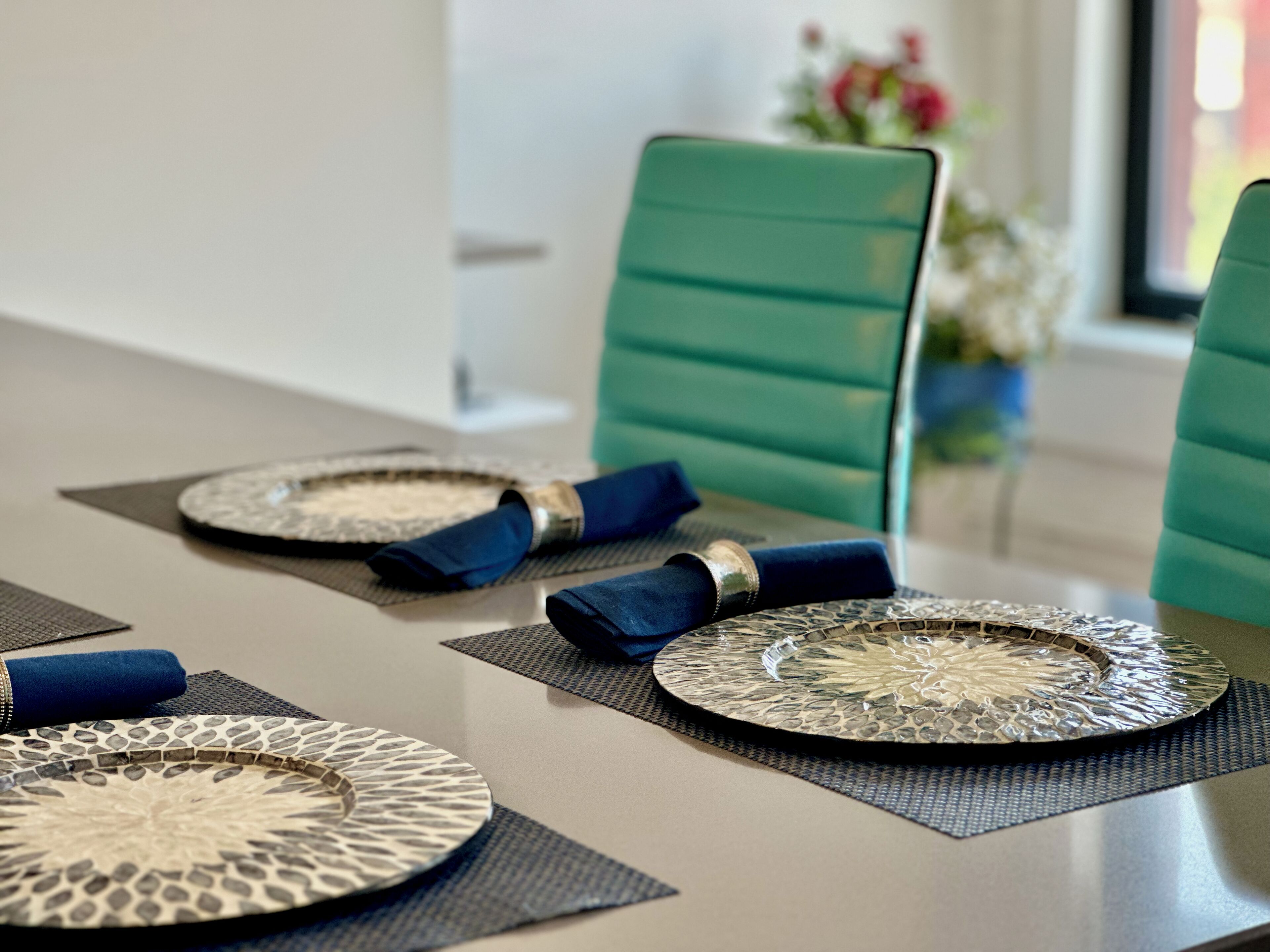 Une table à manger dressée avec des serviettes bleues, des assiettes à motifs et un centre de table décoratif.