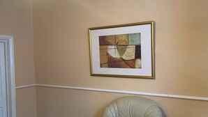 Habitación de esquina con pared color crema, un cuadro abstracto enmarco, un sillón de cuero y una lámpara colgante.