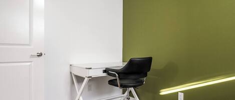 A room with a white desk and black office chair, a green wall, and a white door.