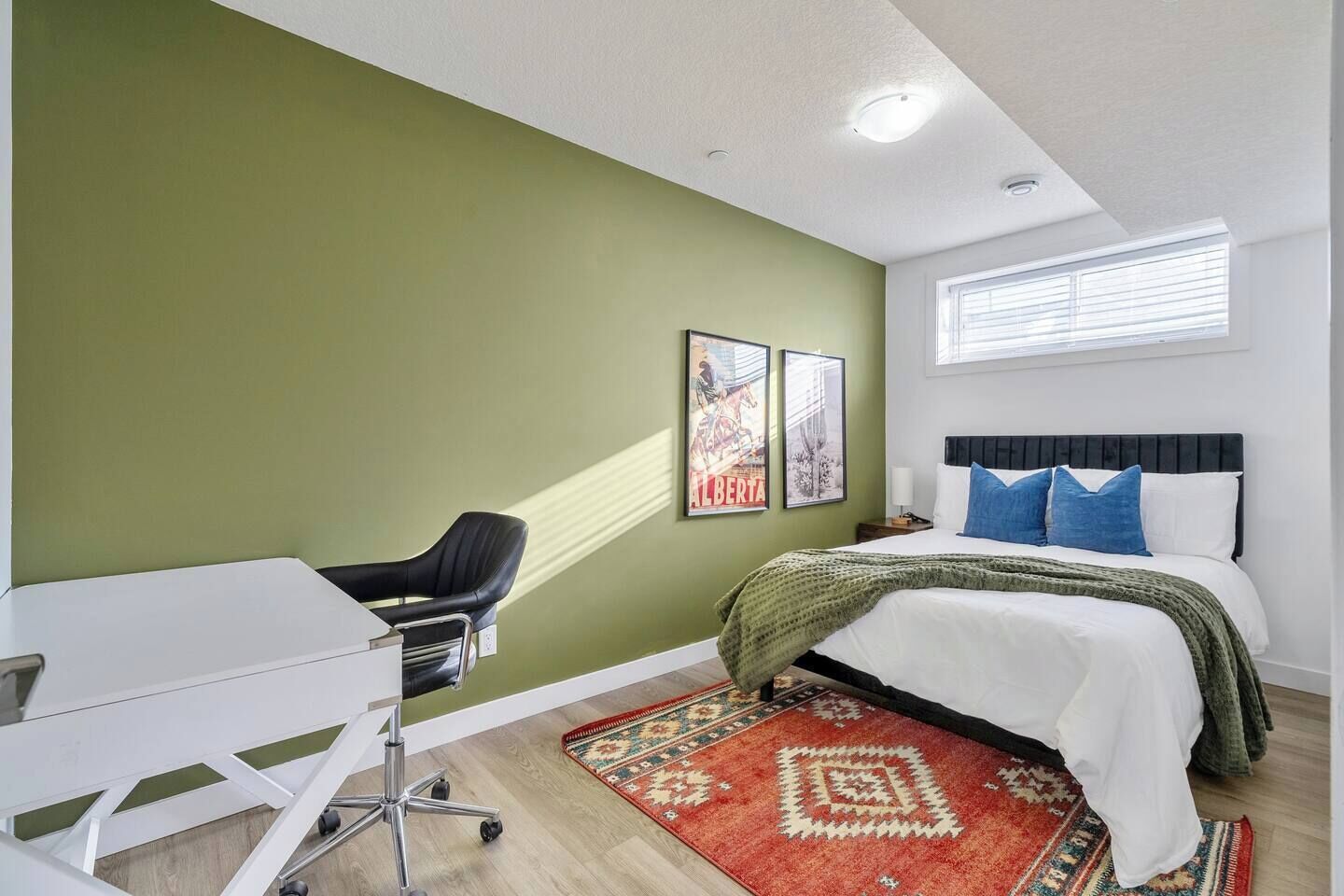 A bedroom with a bed, a desk, and a chair. There are two framed pictures on the wall.