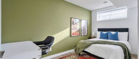 A bedroom with a bed, a desk, and a chair. There are two framed pictures on the wall.