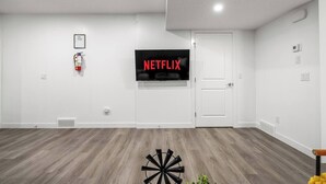 A room with a white wall, a mounted television displaying 'NETFLIX', a white door, and a wooden floor.