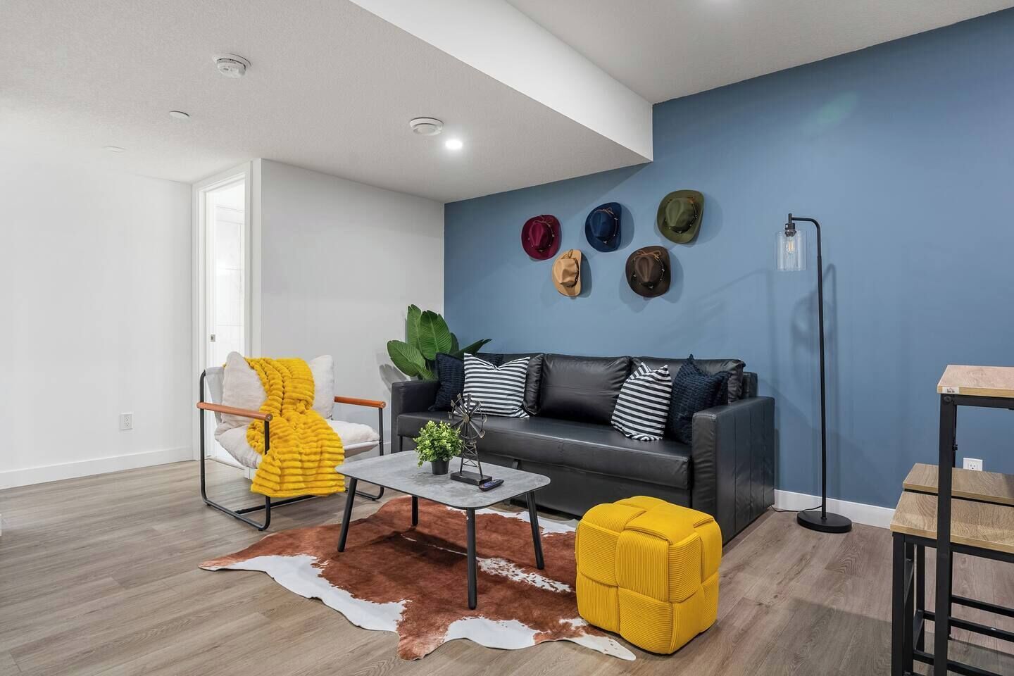 Een moderne woonkamer met een grijze bank, een geel poefje, een salontafel en een koehuidkleed.