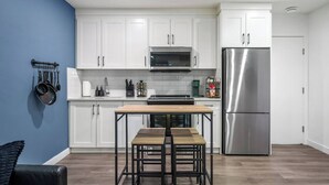 A modern kitchen with white cabinets, a stainless steel refrigerator, a microwave, and a wooden dining table with two chairs.
