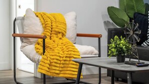 A modern chair with a yellow throw blanket, a small table with a plant, and a windmill decoration.